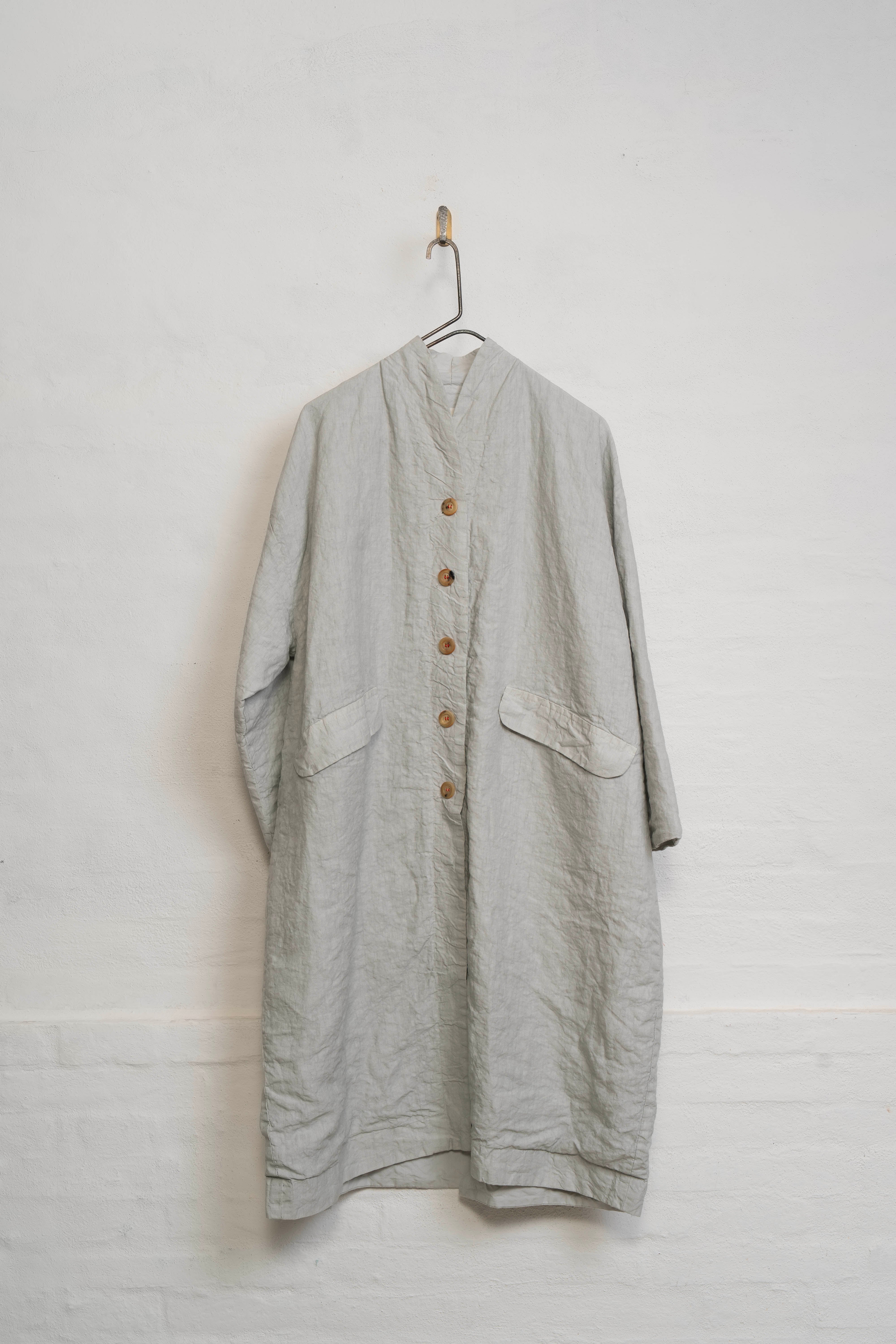 Hannoh Wessel Coat Light gray long-sleeve shirt with buttons on a hanger against a white wall